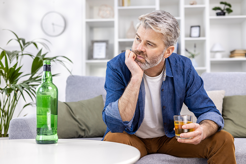 Close up of adult mature man lonely depressed drinking strong alcohol sitting on sofa in living room on day. 